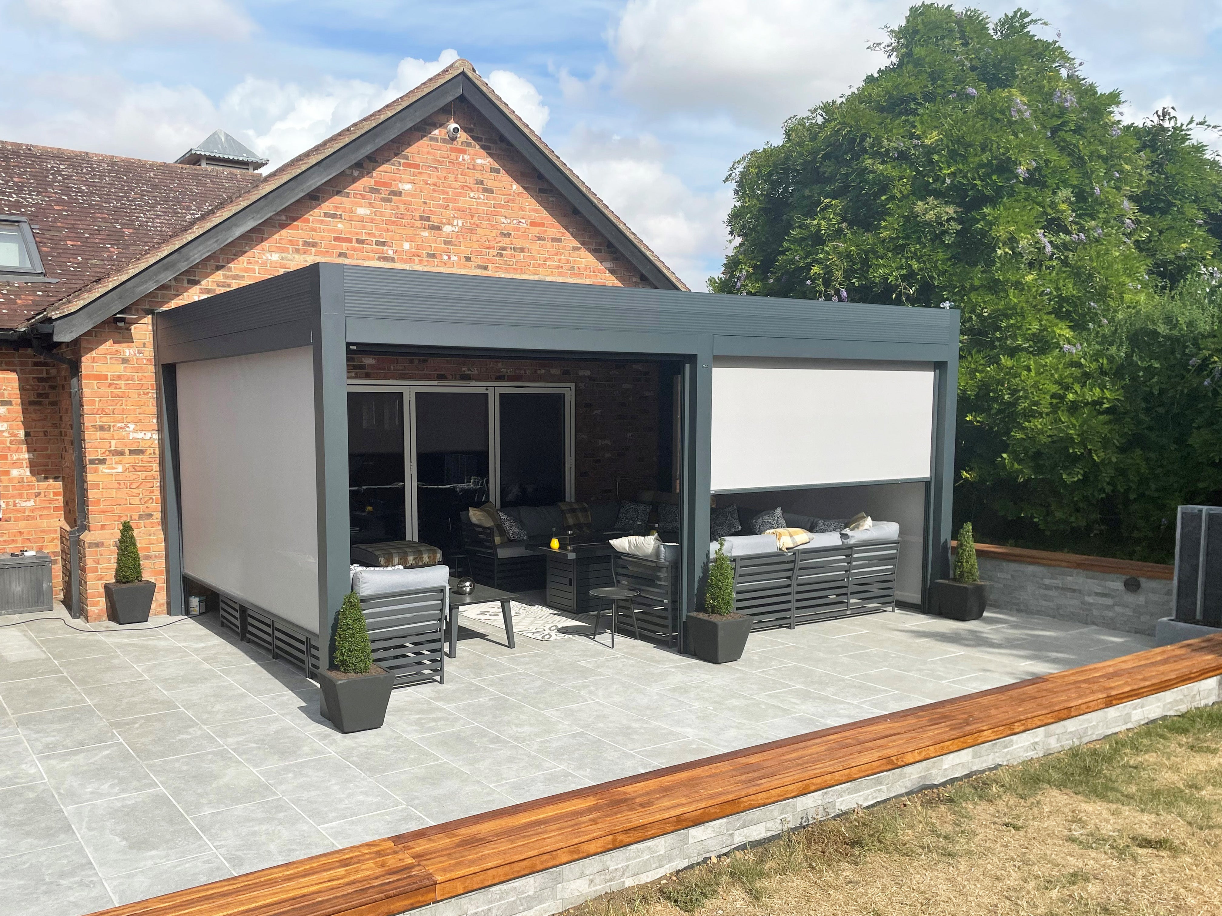 Modern aluminium pergola with retractable roof on a tiled patio, outdoor seating underneath.