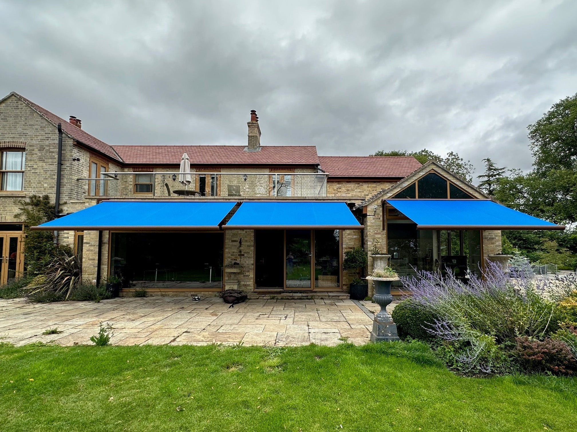 Luxury modern house with blue retractable awnings over patio, surrounded by landscaped garden