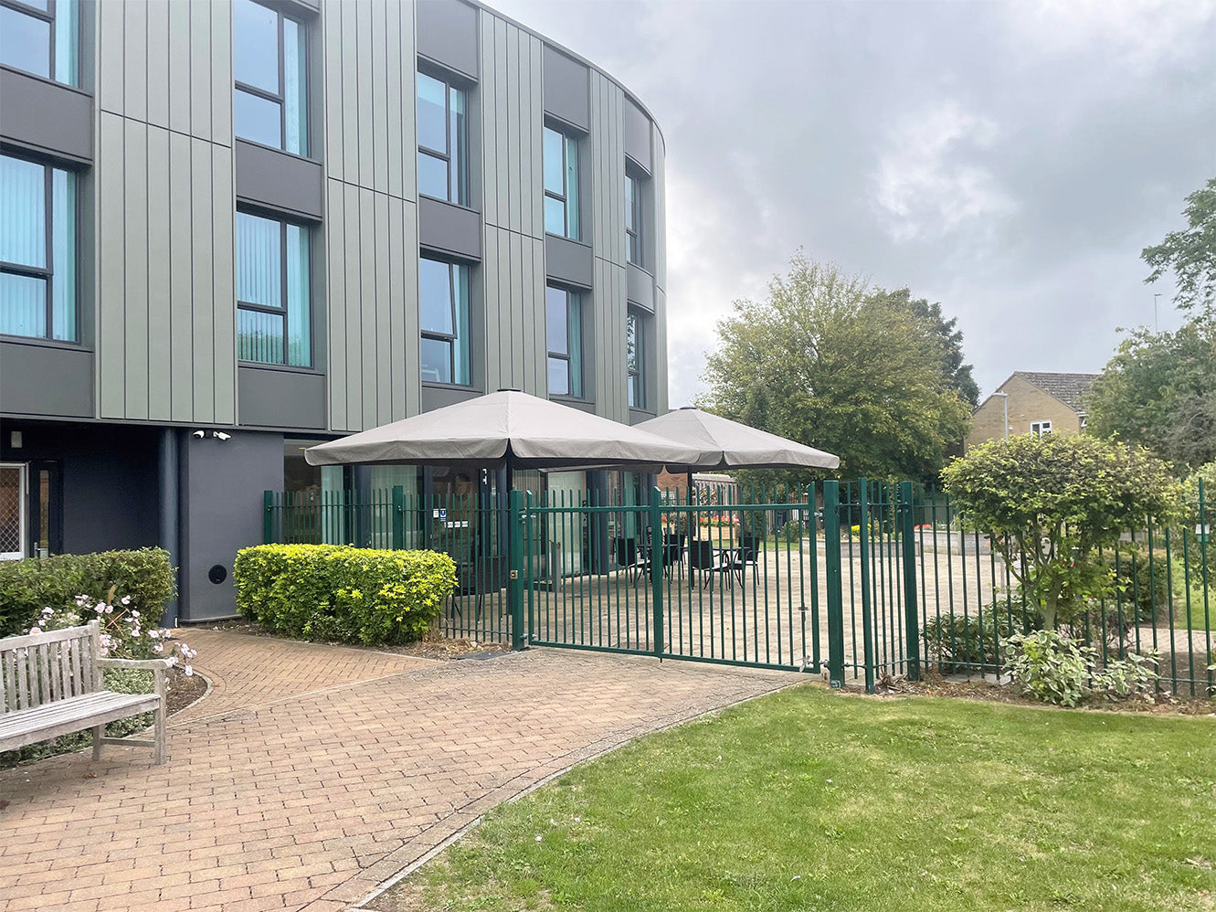 Modern building courtyard with large outdoor luxury umbrellas and green metal fencing