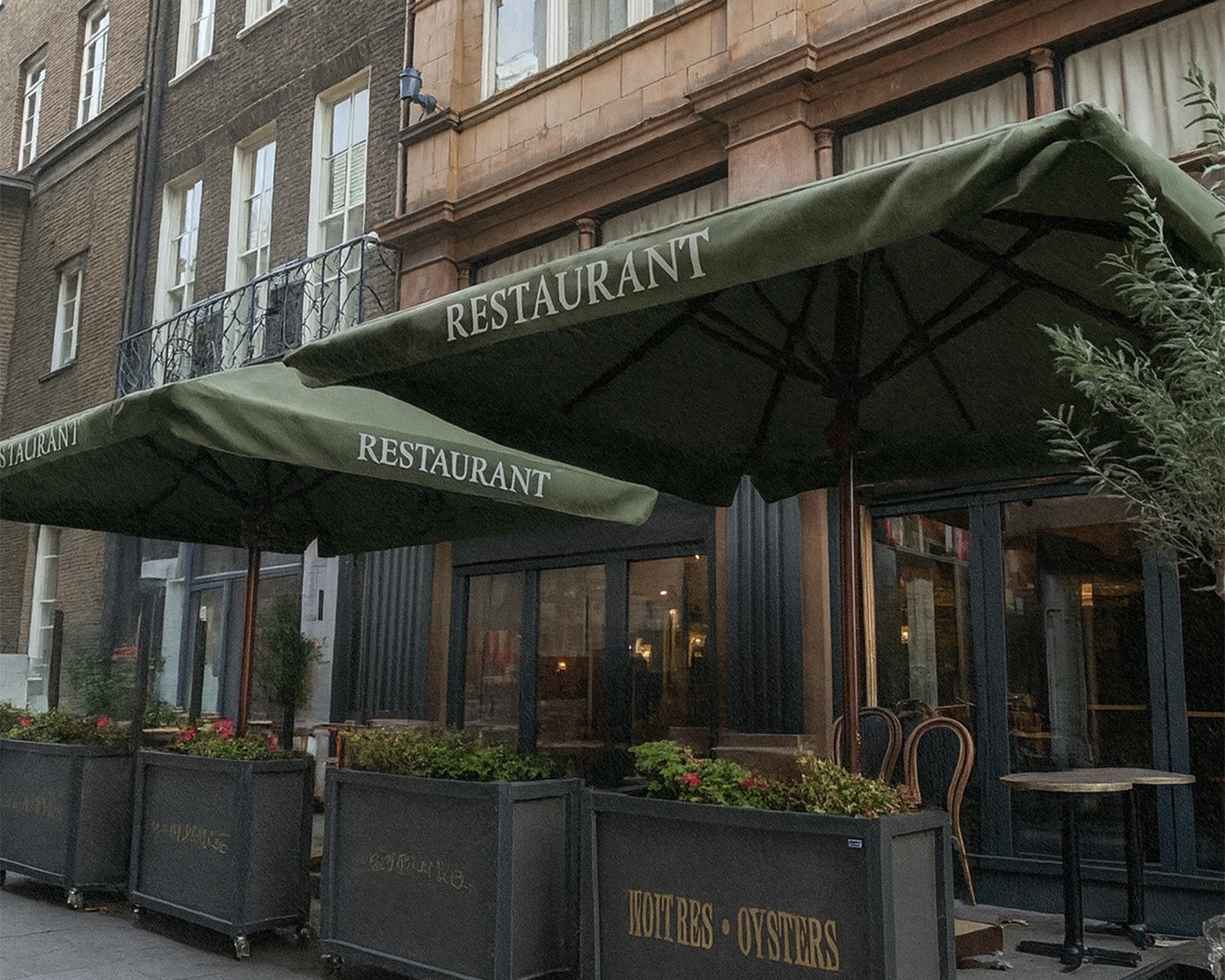 Outdoor restaurant area with large green patio umbrellas and potted plants on city sidewalk