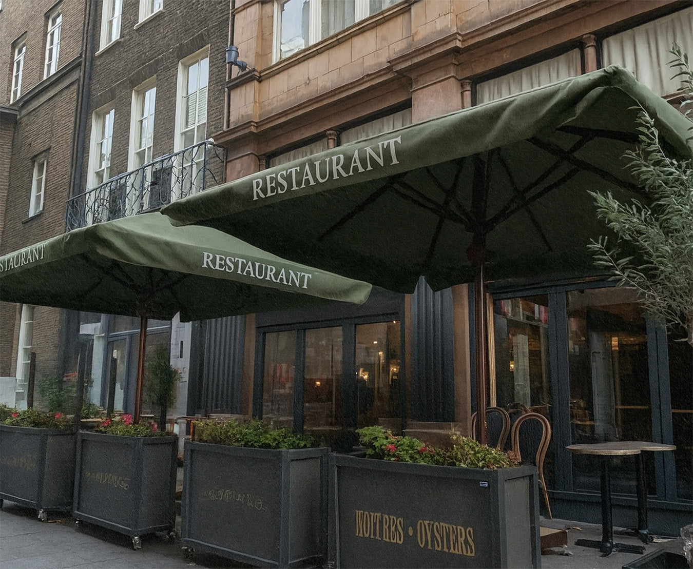 Outdoor restaurant area with large green patio umbrellas and potted plants on city sidewalk