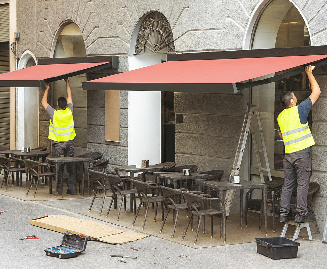 Workers installing modern red awnings over outdoor seating area of a restaurant