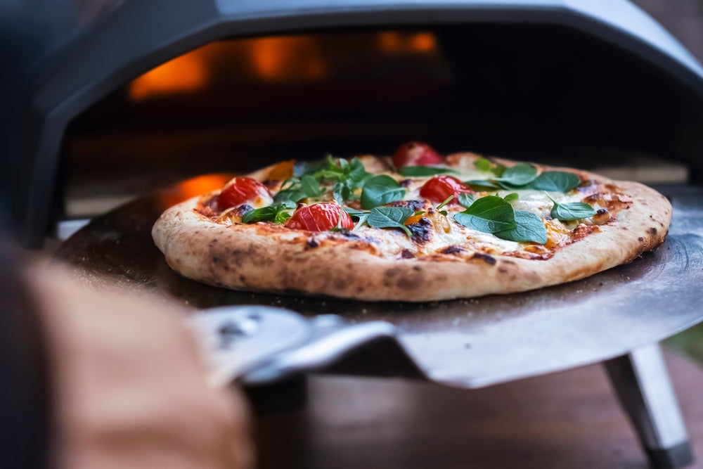 Wood-fired pizza baking in outdoor pizza oven with fresh basil and tomatoes