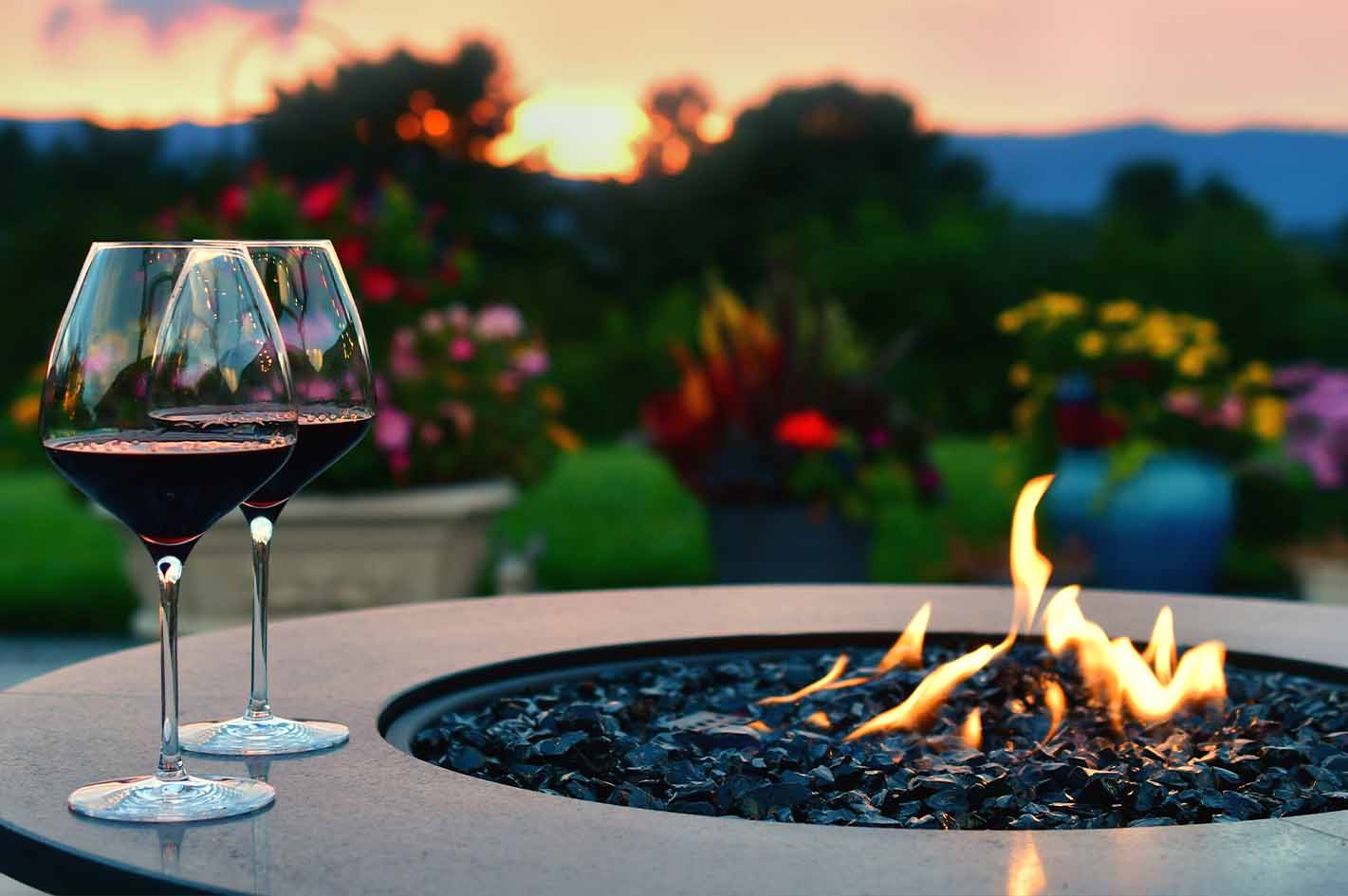 Luxury outdoor fire pit with two wine glasses, colorful flowers, and sunset in garden