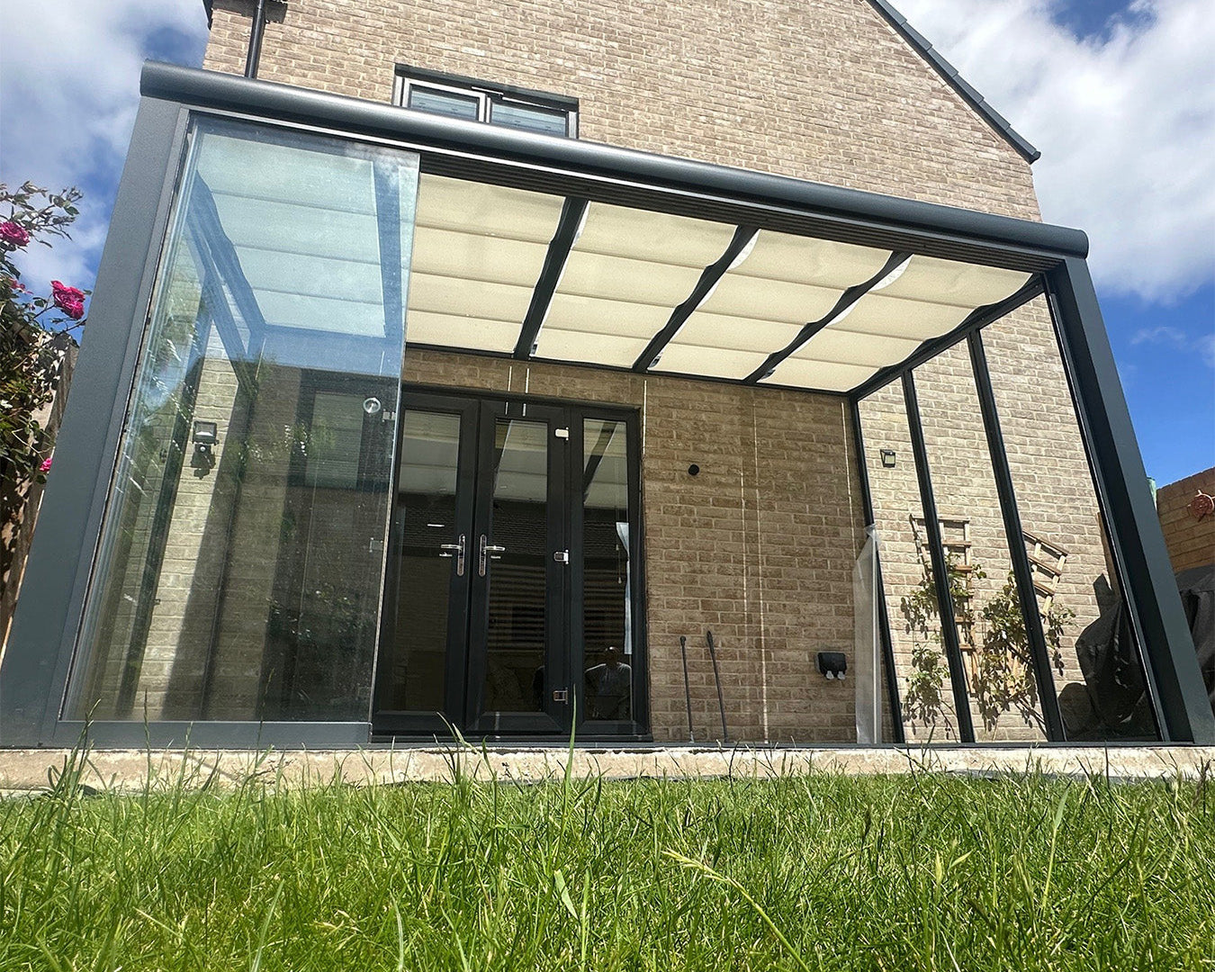 Modern glass and aluminium pergola with retractable roof attached to brick house