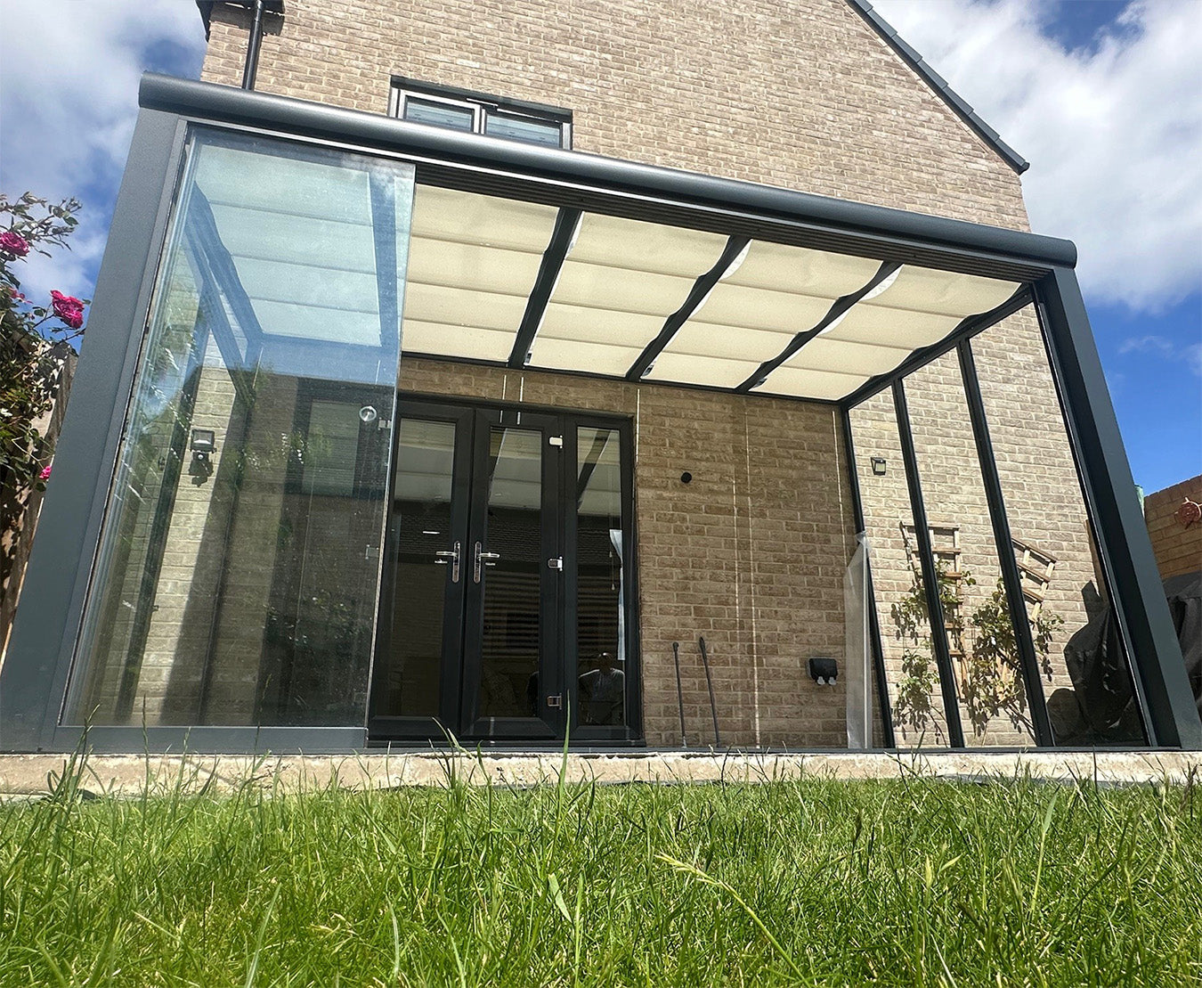 Modern glass and aluminium pergola with retractable roof attached to brick house