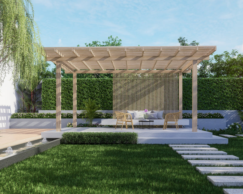 A modern wooden pergola with a slatted back panel in a landscaped backyard, featuring a low seating area with cushions, a small table, a green hedge, lawn, stone steps, and a weeping willow tree.