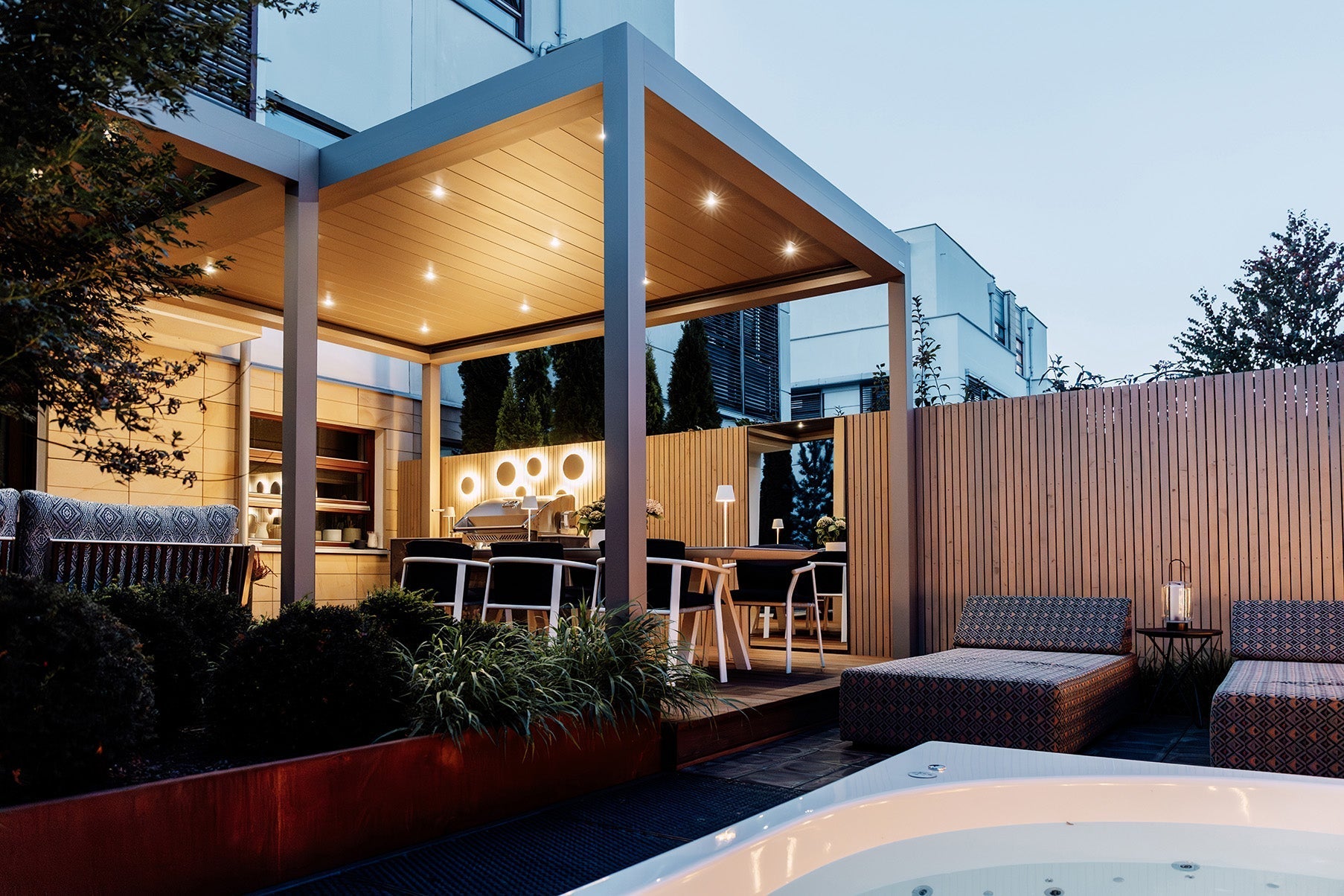 Modern luxury pergola with dining area, outdoor lighting, and jacuzzi in landscaped patio